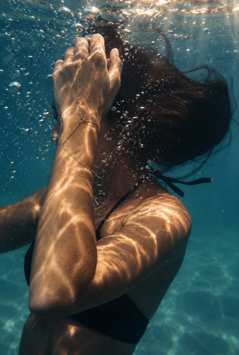 Underwater close-up of a woman in a black bikini, with sunlight filtering through the water and creating shimmering patterns on her skin and hair.